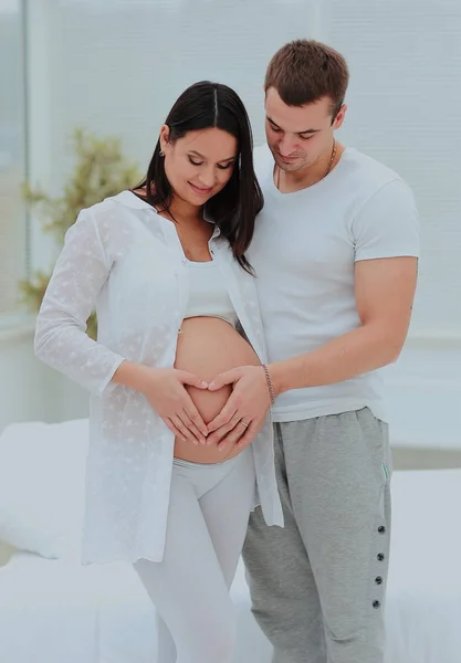 Mann und Frau illustrieren das Herz auf ihrem Babybauch mit den Händen. — Stockfoto