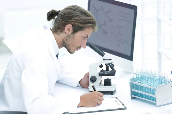 Laboratory worker sitting by table with microscope