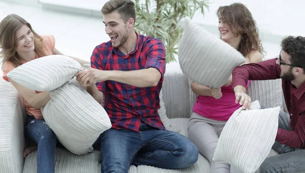 cheerful friends playing pillow fight, sitting on the couch