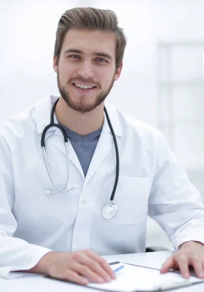 Médico amigável sentado atrás de uma mesa — Fotografia de Stock