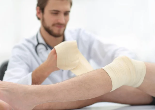 Arzt bandagiert eine Wunde am Bein des Patienten — Stockfoto