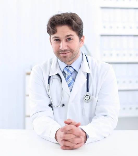 Pohledný mladý lékař v bílém plášti se při pohledu na fotoaparát a usmíval se přitom stát v úřadu — Stock fotografie