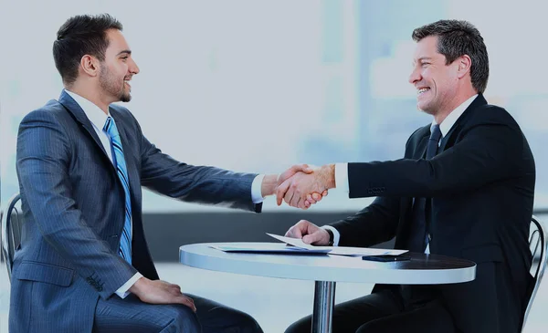 Geschäftskollegen sitzen an einem Tisch während eines Meetings mit zwei männlichen Führungskräften beim Händeschütteln. — Stockfoto