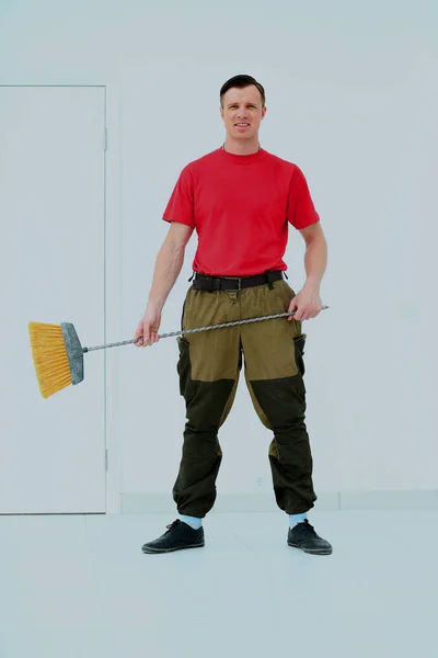 Full length portrait of a cleaner in a uniform with a broom isolated white background. — Stock Photo, Image