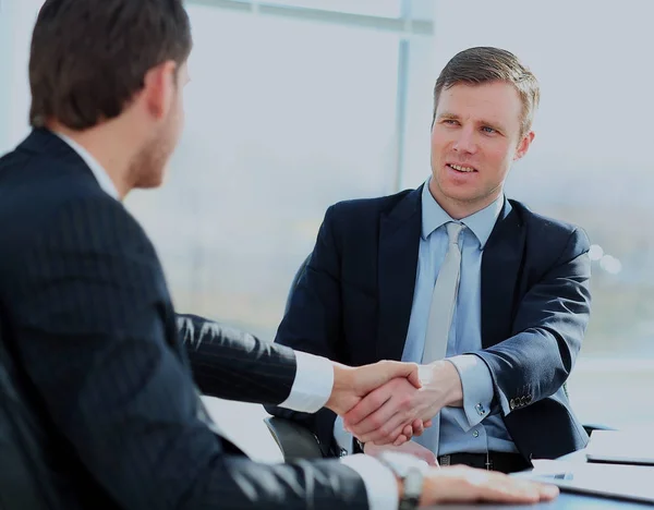 Geschäftskollegen sitzen an einem Tisch während eines Meetings mit zwei männlichen Führungskräften beim Händeschütteln. — Stockfoto