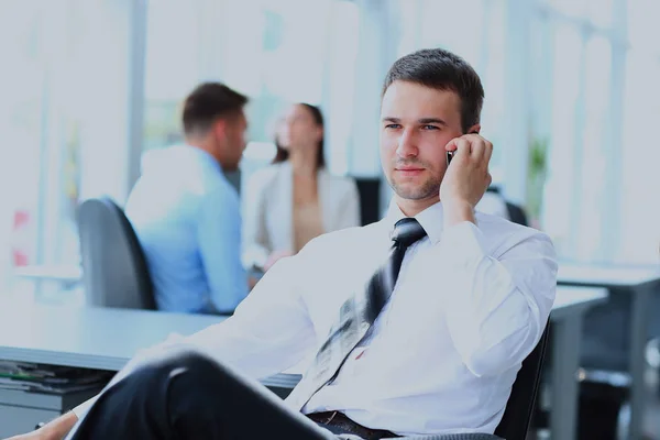 Succesvolle zakenman zit aan zijn bureau tijdens het gesprek op mobiel in office. — Stockfoto