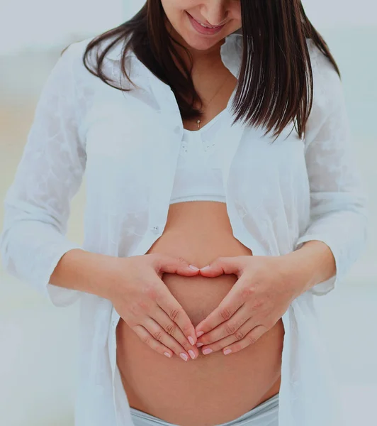 Gravid kvinna visar hjärtat på sin baby bump av händer. — Stockfoto