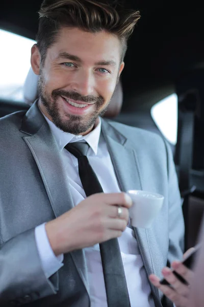 Podnikatel, pití kávy na zadním sedadle auta — Stock fotografie
