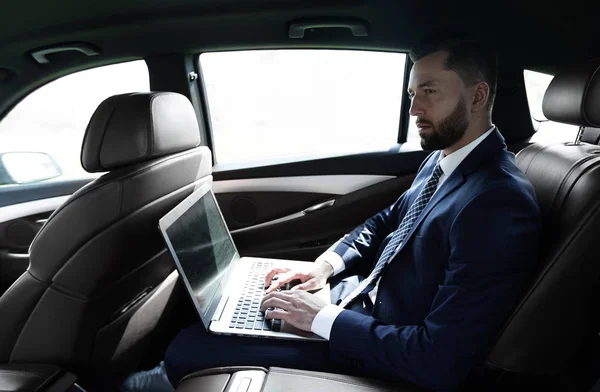 Uomo d'affari che utilizza un computer portatile nel sedile posteriore di una macchina — Foto Stock