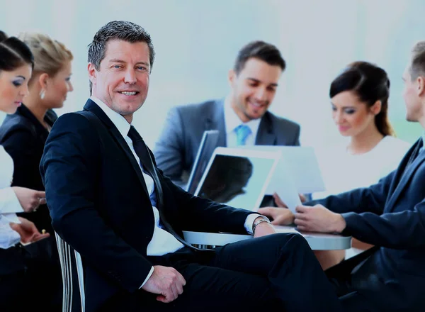 Porträt eines reifen Geschäftsmannes, der bei einem Treffen mit Kollegen im Hintergrund lächelt. — Stockfoto