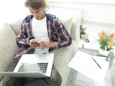 dizüstü bilgisayar ve akıllı telefon oturma odasında ciddi genç adam.