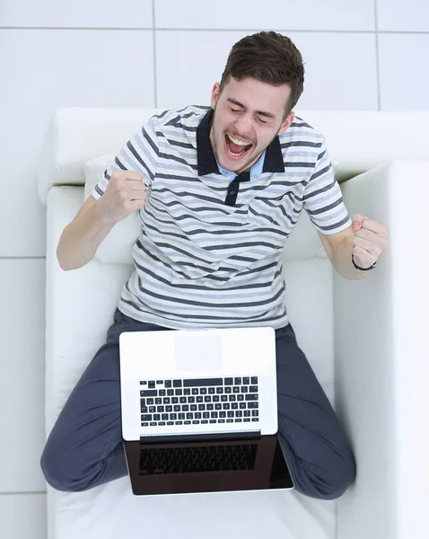 Pohled z vrcholu. jásavý mladý muž s notebookem sedět na gauči — Stock fotografie