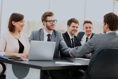 İki emin işadamları el sıkışma ve kendi meslektaşları ile birlikte masada otururken gülümseyen.