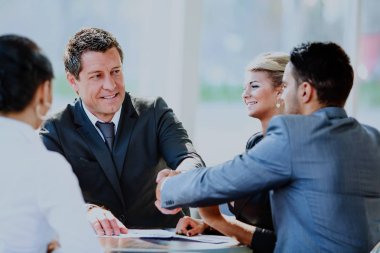 Olgun iş adamı, modern bir ofiste ortağı ve iş arkadaşlarıyla anlaşma yapmak için el sıkışıyor..