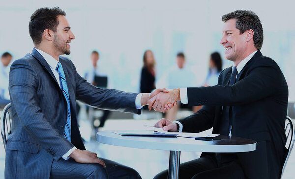 Compañeros de negocios sentados en una mesa durante una reunión con dos ejecutivos masculinos dándose la mano . — Foto de Stock