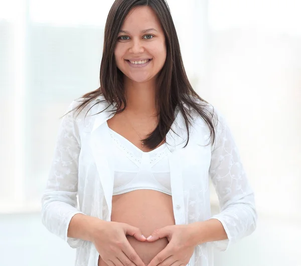 Gyönyörű terhes nő fogja kéz a szív alakját a hasán. — Stock Fotó