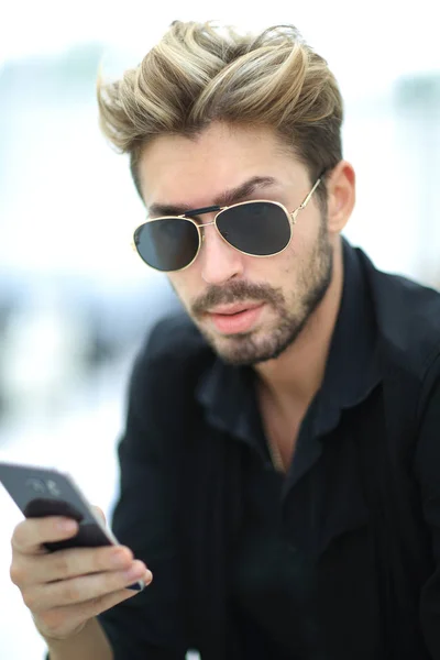Ein stylischer bärtiger Mann sitzt und benutzt ein Smartphone. — Stockfoto
