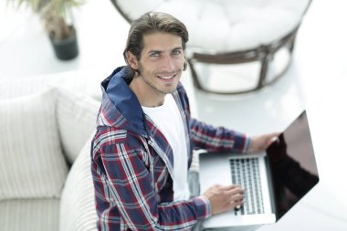 dizüstü bilgisayarda çalışan ve kameraya bakarak bir genç adam. Yukarıdan görüntülemek