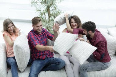 Bir grup arkadaş yastık savaşı yapıyor, kanepede oturuyor.