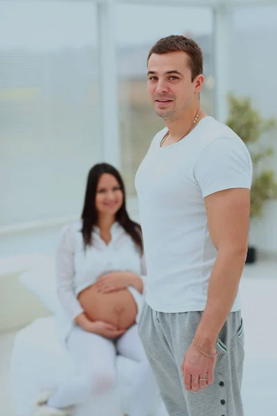 Ein Mann steht im Schlafzimmer, im Hintergrund sitzt seine schwangere Frau. — Stockfoto