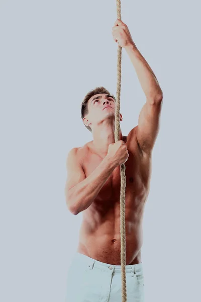 Junger Mann versucht, Seil zu klettern und schaut isoliert auf weißem Hintergrund nach oben. — Stockfoto