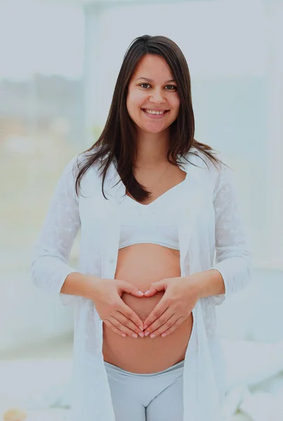 Zwangere vrouw toont het hart op haar baby bump door handen. — Stockfoto