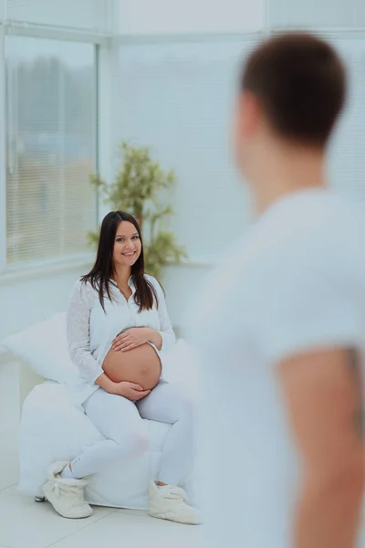 the man turned back to his pregnant wife, who is sitting on a bed.