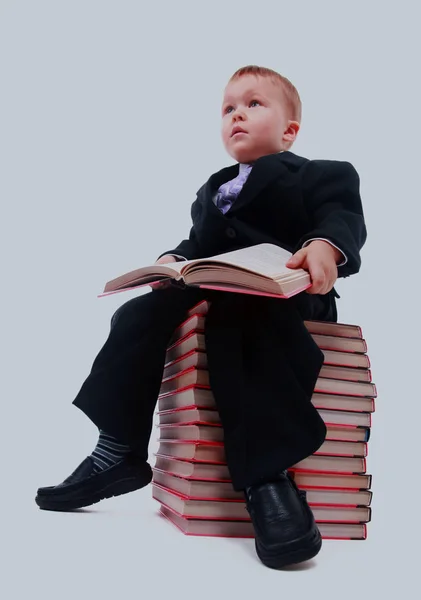 Porträt eines asiatischen Schuljungen, der ein Buch in der Hand hält und auf einem Stapel Bücher sitzt, isoliert auf weißem Papier. — Stockfoto