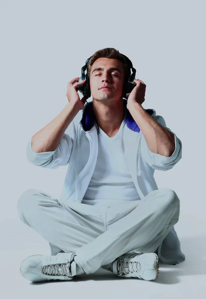 Porträt eines entspannten jungen Mannes, der Musik über Kopfhörer vor weißem Hintergrund hört. — Stockfoto