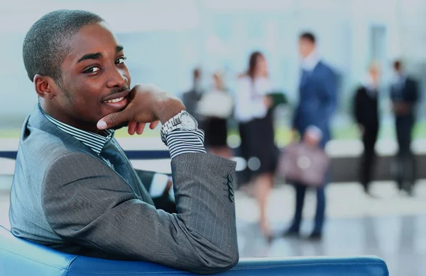 Porträtt av leende amerikansk affärsman med chefer som arbetar i bakgrunden. — Stockfoto