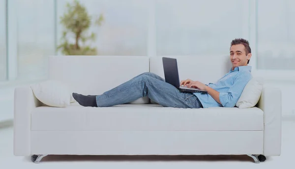 En man liggande på soffan arbetar på datorn. — Stockfoto