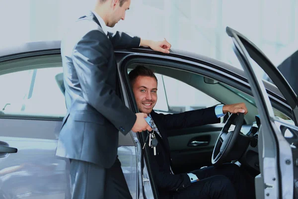 Joven hombre elegir el coche en el salón con la ayuda de un consultor . — Foto de Stock