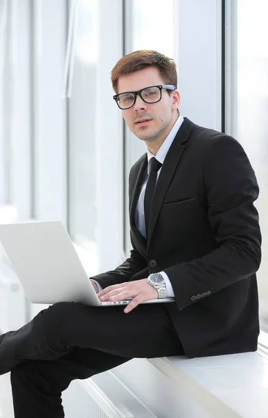 Молодой профессионал с ноутбуком на фоне офисного окна — стоковое фото