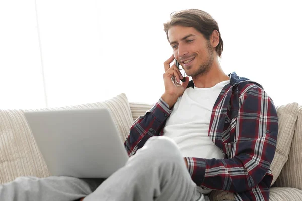 Serious young man with laptop talking on mobile phone — Stock Photo, Image