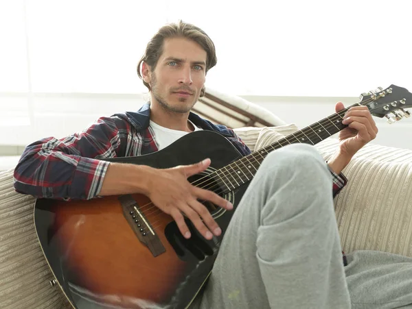 Cara moderno com guitarra sentado no sofá na sala de estar . — Fotografia de Stock