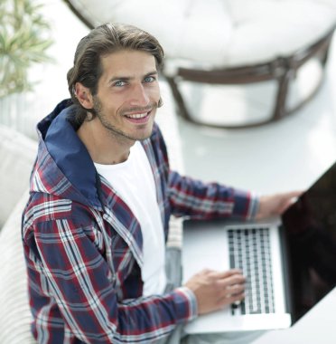 dizüstü bilgisayarda çalışan ve kameraya bakarak bir genç adam. Yukarıdan görüntülemek