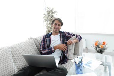 genç adam bir sehpa yakınındaki bir kanepede oturan bir dizüstü bilgisayar ile