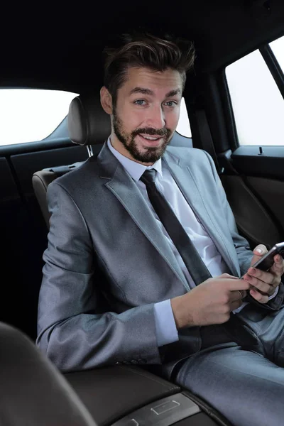車に座っていると、スマート フォン上のメッセージを読んでのスーツを着た男 — ストック写真