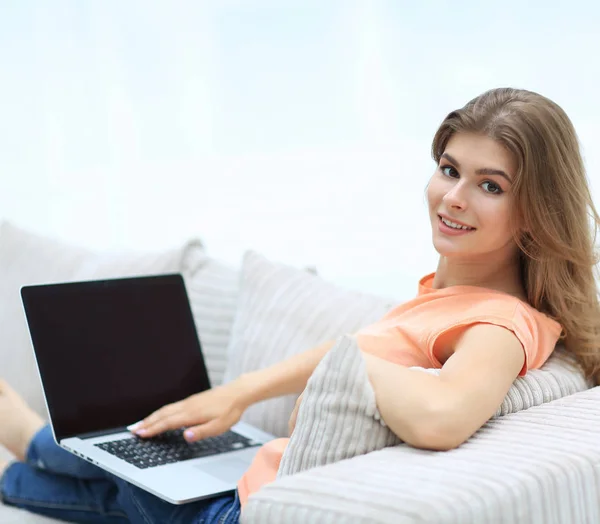 Mooie jonge vrouw die werken met de laptop op de bank zitten en kijken naar camera. — Stockfoto