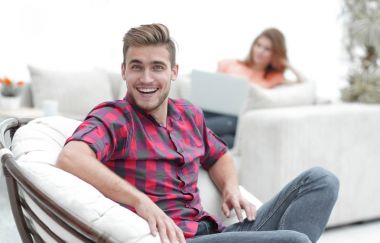 Bulanık arka planda büyük bir sandalyede oturan mutlu genç adam.