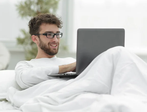 Bell'uomo che lavora sul computer portatile sdraiato sul letto — Foto Stock