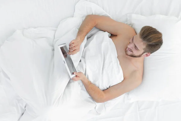 Lächelnder Mann mit digitalem Tablet im Bett liegend — Stockfoto