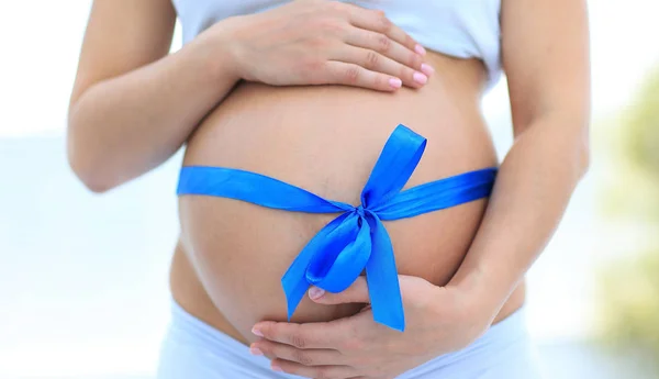 Close-up van een zwangere vrouw koppelverkoop een blauw lint op haar buik — Stockfoto