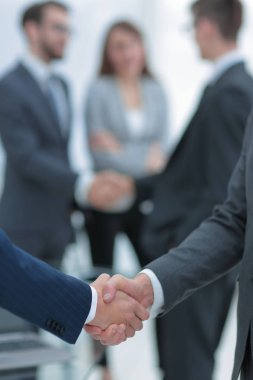 İki iş adamı arka planda meslektaşlarıyla tokalaşıyor..