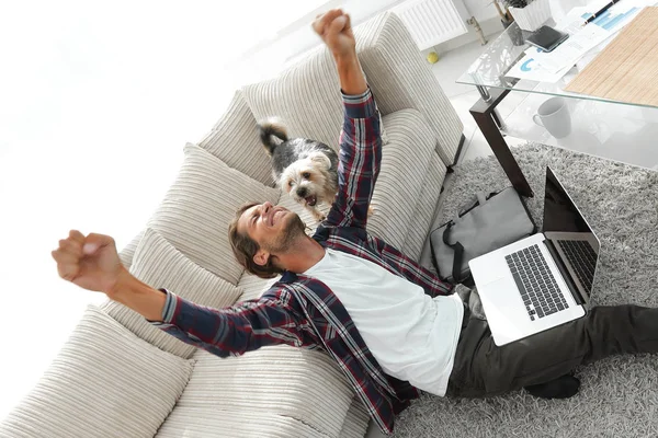 Geniş bir oturma odasında otururken köpeğiyle mutlu adam — Stok fotoğraf