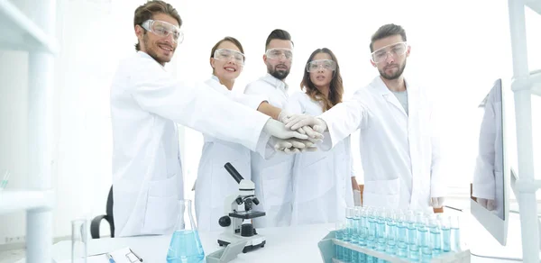 Erfolgreiches Team junger Wissenschaftler mit zusammengeklammerten Händen. — Stockfoto