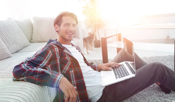 Charmanter junger Mann mit Laptop sitzt im modernen Wohnzimmer — Stockfoto