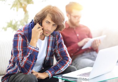 adam kanepede oturan, belgili tanımlık smartphone üzerinde konuşmak ve internette bilgi arayan bir arkadaşıyla.