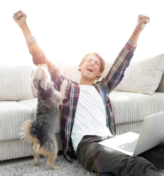 Glad ung man jublar med sin hund som sitter i vardagsrummet — Stockfoto