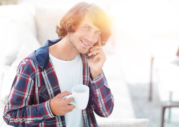 Hermoso chico con una taza se sienta delante de un ordenador portátil . — Foto de Stock